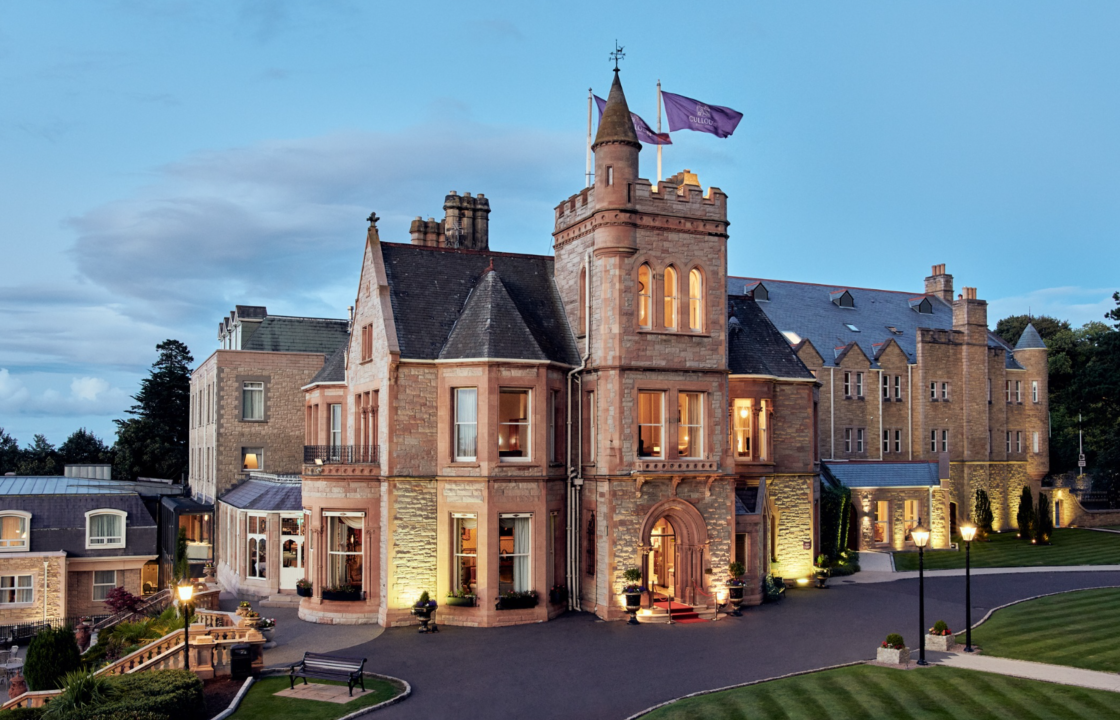 A grand historic mansion with warm lighting and manicured gardens at dusk.